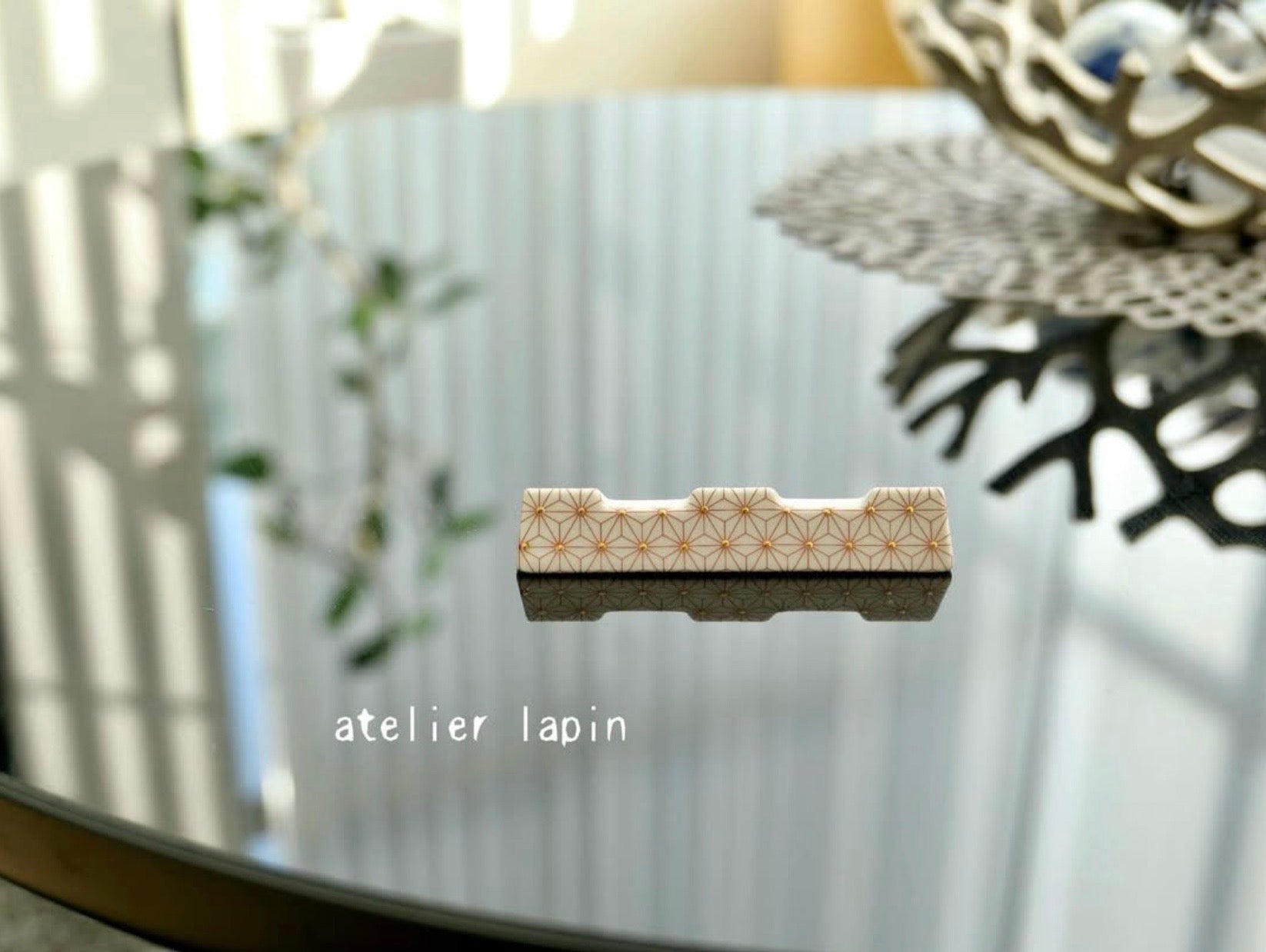 和モダンなポーセリンアートの箸置き。有本信子さんが主宰する西宮のサロン「atelier lapin（アトリエ・ラパン）」制作。伝統的な麻の葉文様を繊細な金彩で表現した磁器作品。SAKURA JAPANの帯を切らずに飾る額縁と調和する、洗練されたおもてなしの小物実例。